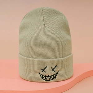 Detailed close-up of beige knit beanie featuring black embroidered quirky ghost face pattern