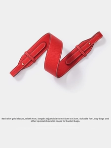 Macro detail of red lychee leather shoulder strap with white stitching and gold hardware