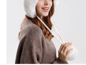 Close-up of white plush earflap hat with faux fur texture and decorative pom-poms