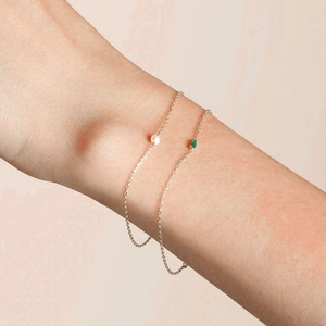 Detail of silver chain bracelet set featuring green zircon and white pearl on wrist