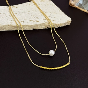 Detail view of a double-layered gold necklace featuring a white pearl and a textured metal tube