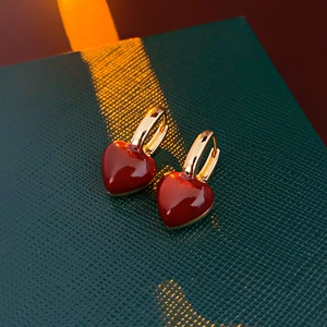 Detailed close-up of small red enamel heart earrings with gold metal clasp on gift box