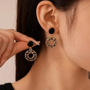 Gros plan d'un mannequin portant des boucles d'oreilles dorées avec détails noirs et cristaux