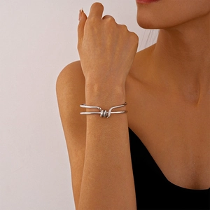 Detail view of a silver double-layered knotted geometric cuff bracelet on a female wrist