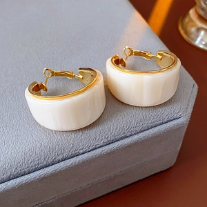 Macro view of gold plated C-shaped resin hoop earrings with wide white glossy finish