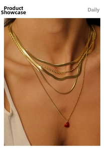 Close-up of gold-plated layered necklaces featuring a red heart pendant and sleek snake chain