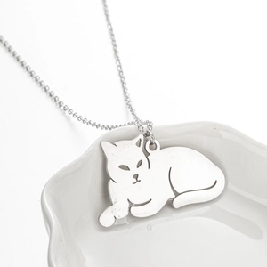 Collier minimaliste avec pendentif chat allongé argenté sur une assiette blanche
