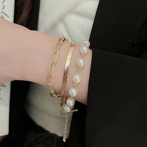 Detail of layered gold bracelet set with paperclip chain, snake chain, and white pearls