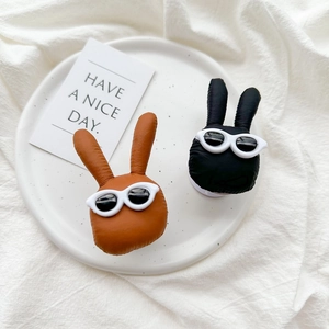Detail of plush rabbit phone grips with sunglasses in black and brown on a ceramic tray