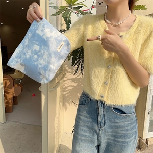 Close-up of blue tie-dye toiletry bag with brand label held by person in yellow sweater