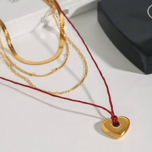 Close-up of a red cord necklace with a golden heart pendant and layered chains