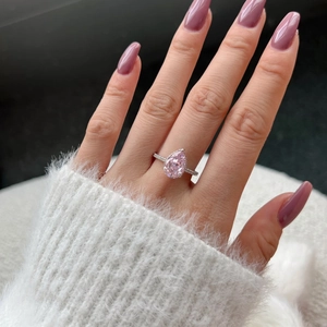 Macro view of pear-cut pink gemstone ring with pavé diamond band on a white background