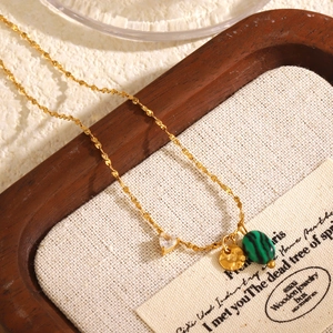 Collier doré avec pendentif en zircon cœur et malachite sur plateau en bois