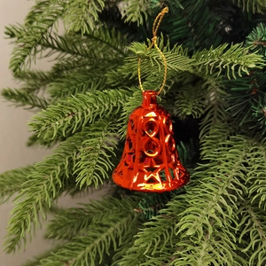 Detail eines roten Weihnachtsklingel-Anhängers mit Sternmuster an Tannenzweigen