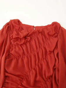 Close-up of red pleated mesh fabric detailing the elegant texture of the long sleeve dress