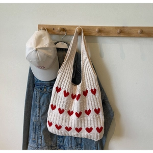 Primer plano de un bolso tote de punto crema con corazones rojos colgado en un gancho