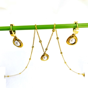 Golden necklace and hoop earrings set with round white pearls on a green display rod