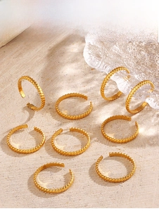 Detail of 18K gold plated twisted rope rings on textured stone and water glass