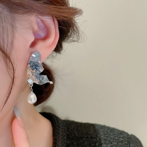 Close-up of butterfly earring with blue crystals and a white pearl on a model's ear