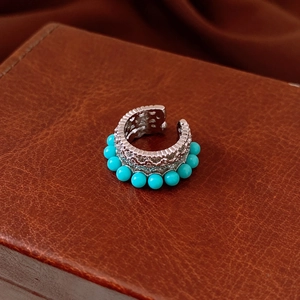Detail view of retro silver ear cuff with hollow pattern and green turquoise beads