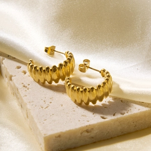 Detail of gold textured C-shape hoop earrings on a stone with elegant silk background