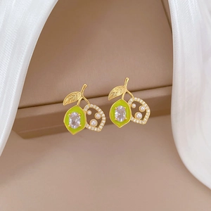 Detail of gold fruit earrings with green enamel, clear zircons and white pearls on satin