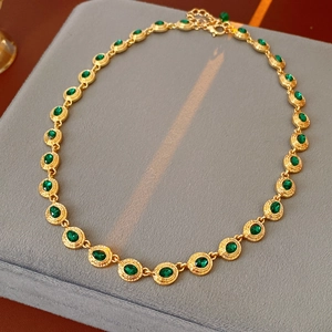 Détail d'un collier vintage doré avec pierres vertes sur un coffret en velours