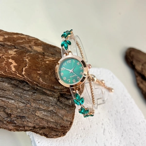 Detail of green dial quartz watch with rose gold leaf bracelet on natural wood