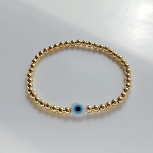Macro detail of gold beaded stretch bracelet featuring a blue lucky evil eye charm bead