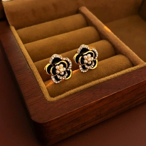 Detailed macro of golden flower earrings with black petals, crystals, and pearls