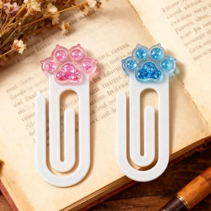 Macro detail of glitter-filled pink and blue cat paw bookmarks on vintage book pages