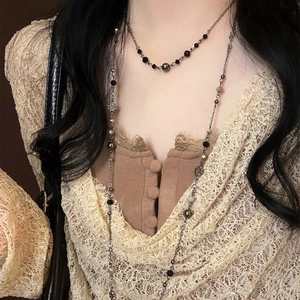 Detail of double-layered beaded necklace with black beads and silver flower pendant on a model