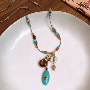 Dettaglio collana boho con pendente in turchese e perline di legno su ceramica bianca