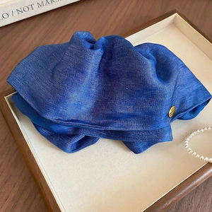 Close-up of royal blue pleated fabric hair claw with golden metal logo in a wooden tray