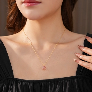 Close-up of gold plated necklace with a round pink crystal pendant on model neck
