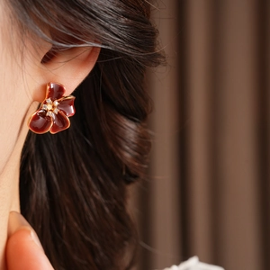 Close-up of a red enamel flower earring with metal edges and small diamonds on a model
