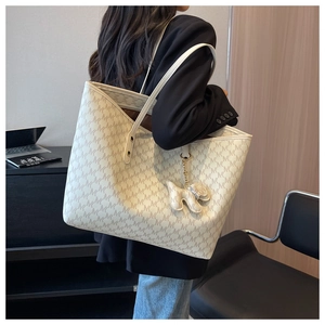 Detailed view of cream tote bag with logo print and dog-shaped hanging charm on model