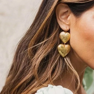 Vintage gold layered heart earrings with floral texture worn by a fashion model
