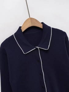 Detail of navy knit cardigan featuring contrast white scallop trim and round black buttons