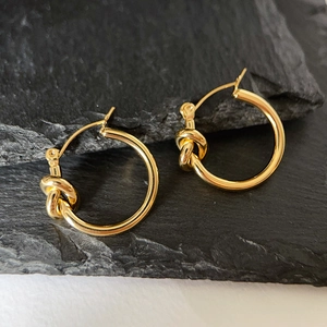 Detail shot of 18k gold plated stainless steel knot hoop earrings on a black stone