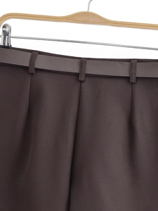 Detailed view of dark brown pleated trousers with matching synthetic leather waist belt