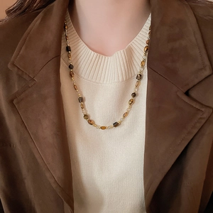 Détail d'un collier en œil de tigre avec perles brunes sur un mannequin en veste