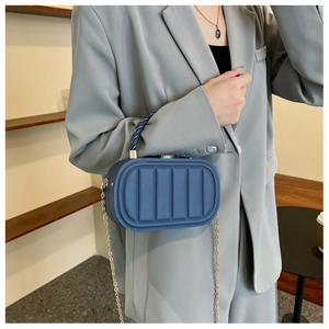 Detail of blue quilted box bag with chain strap and top handle shown on a grey suit