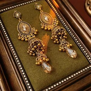Détail de boucles d'oreilles vintage dorées avec cristaux champagne sur velours vert