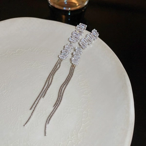 Macro view of silver tassel earrings featuring step-cut crystals and triple chain details