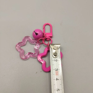 Pink acrylic star keychain with bell and plastic clasp shown with a measuring tape