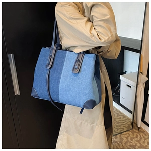 Detailed view of dual-tone blue denim tote bag with leather handles on a model