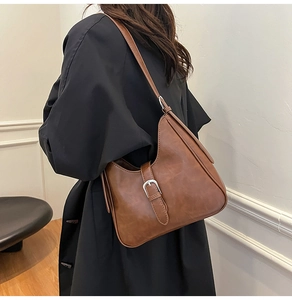 Détail d'un sac à bandoulière marron foncé texturé avec une boucle métallique élégante