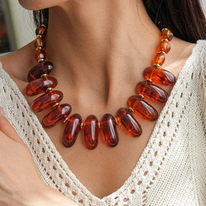 Vue détaillée d'un collier en résine ambre avec perles dorées porté par un mannequin