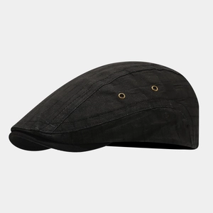 Detailed view of black newsboy cap with subtle check texture and golden eyelets